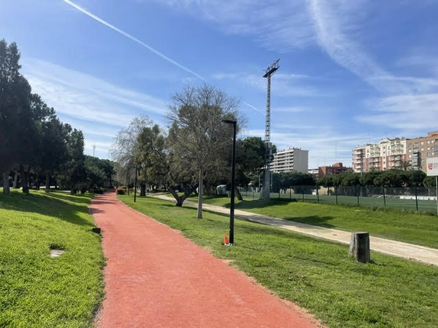 Caminho vermelho entre relvados e árvores do jardim